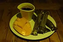 画面左上角是一杯巧克力,杯口两侧较低。左下角是半个吕宋芒,切成小块,并翻成拱形。右侧是长条形、用叶子包裹的糯米甜品苏曼。