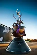 一座大型金属纪念碑,扭曲的乐器包裹着地球。背景是蓝色天空。