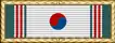 White ribbon with vertical green and red stripes on its edges and a red and blue circle in the middle