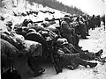 A convoy in the .snow with men resting on the vehicles