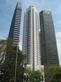 Ground-level view of three 40-storey towers. The building on the left is very thin with a blue and grey facade. The building in the center has a square cross section with diagonal, cut-off corners and a tapering roofline. The building on the right is box-like with diagonal corners and a brown facade.