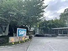 树荫下,一处建筑前的庭院,左侧有一个蓝底白字的“SAP”标志