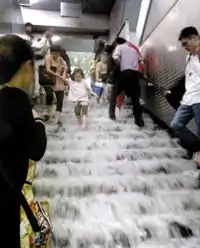 面前是一个楼梯,大量水从上往下流,形成了一个个小“瀑布”,整个楼梯被白色的水花覆盖。一位母亲领着小女儿在楼梯上小心翼翼地下行。